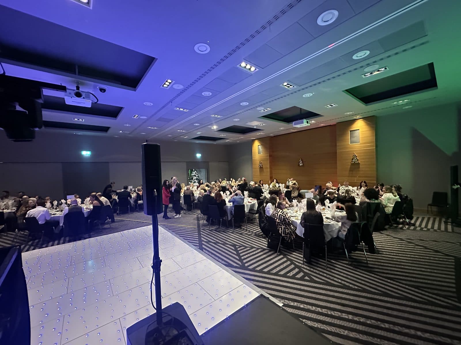 The function room at the Radisson Blu, London Stansted Airport, laid for dinner, with the DJ booth and lighting set up beside the dancefloor